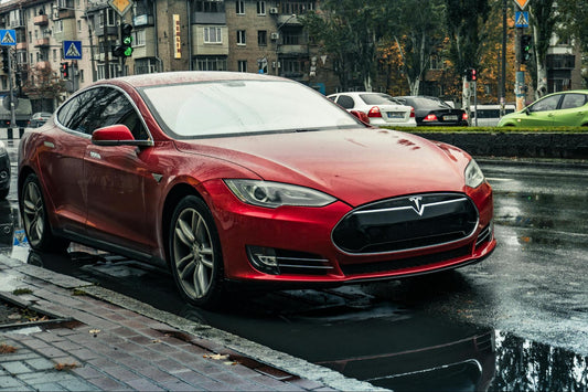 Red Tesla Model S parked on a rainy street.